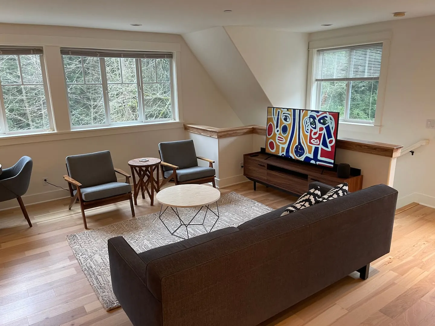 Living room with a 55-inch TV, mid-century armchairs and large wooded-view windows